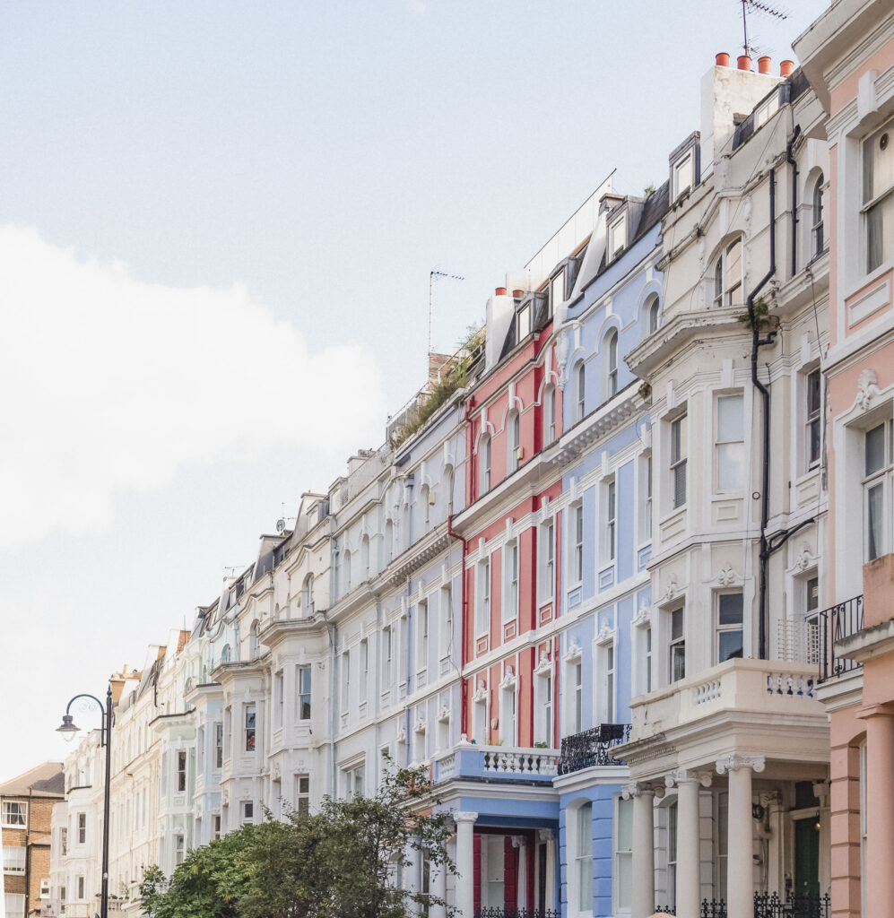 Row of pastel London townhouses — blue, pink, white — catching soft afternoon light.